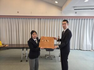 生徒にアイゴを寄贈している写真。アイゴには碁石で点字の「いばらき」と書いてあります。